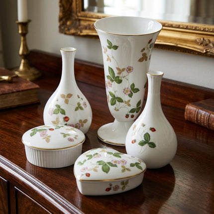 A set of five white porcelain decorative items with a delicate pink and green strawberry floral pattern and gold trim, including a tall vase, two smaller vases, a lidded box, and a heart-shaped box, photographed on a light gray background.