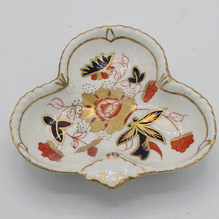 A vintage three-part ceramic petal dish with a white glaze, decorated with gold, red, and navy blue floral and butterfly motifs, set against a plain light gray background.