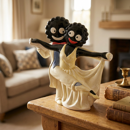 A decorative figurine of two dancing figures, one with black skin and cream dress and one with dark curly hair and cream dress, displayed on a wooden table in a softly blurred living room setting.