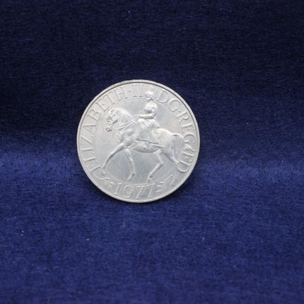 Silver Queen Elizabeth 1977 coin with the queen on a horse on a blue fabric background