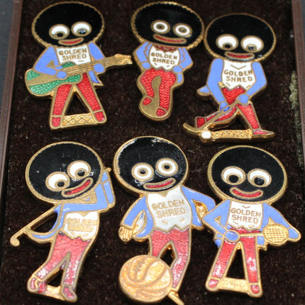 Set of six Golden Shred golliwog pins on a dark background