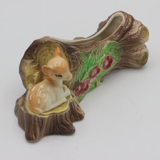 A ceramic decorative dish shaped like a tree stump with a small fawn figurine sitting inside, featuring painted green leaves and pink flowers on a light gray background.