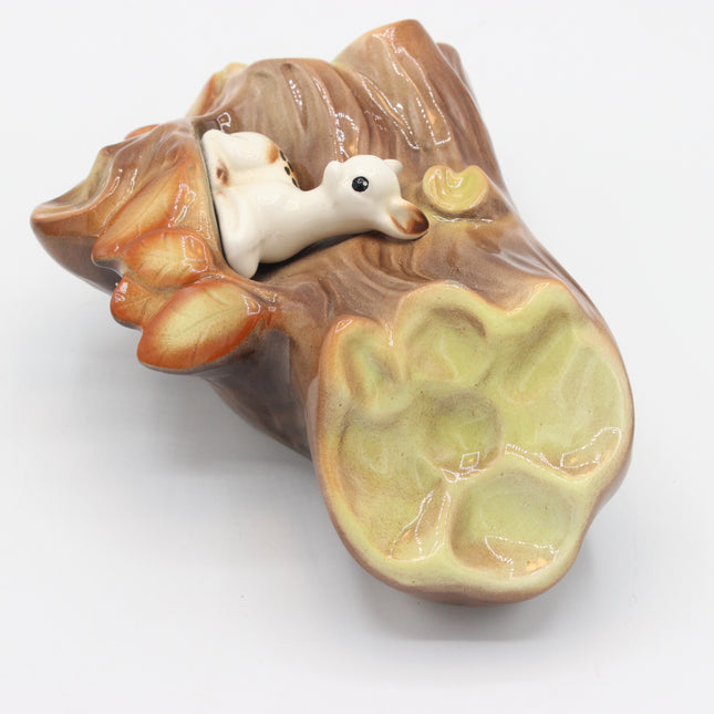 A ceramic woodland-themed dog bowl shaped like a tree trunk, featuring a small white dog figurine on top and a green paw-print shaped insert at the front, shown on a plain white background.