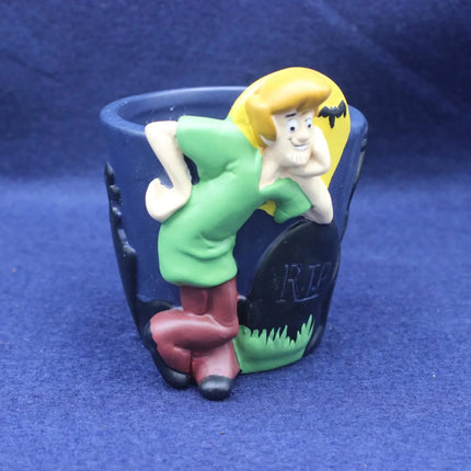 A novelty pot featuring a cartoon Shaggy character leaning over a tombstone with 'RIP' written on it, set against a dark blue background.
