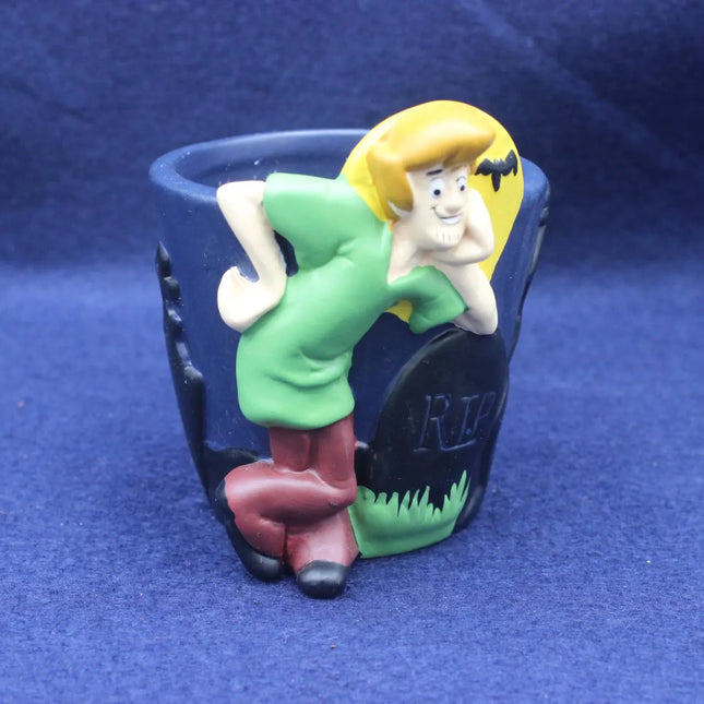 A novelty pot featuring a cartoon Shaggy character leaning over a tombstone with 'RIP' written on it, set against a dark blue background.