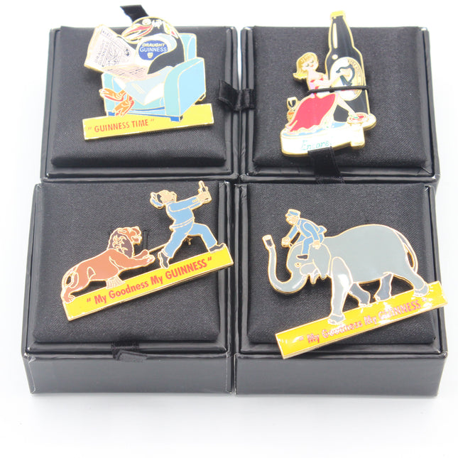 Four enamel pin badges featuring Guinness-themed characters and logos, displayed on a black velvet grid with black presentation boxes.