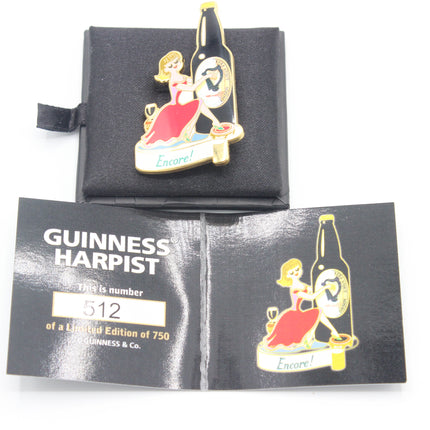 A vintage Guinness Harpist enamel pin displayed on its black presentation card, with a second card showing the limited edition number 512. The pin features a woman in a red dress next to a beer bottle with the word 'Encore' at the bottom.