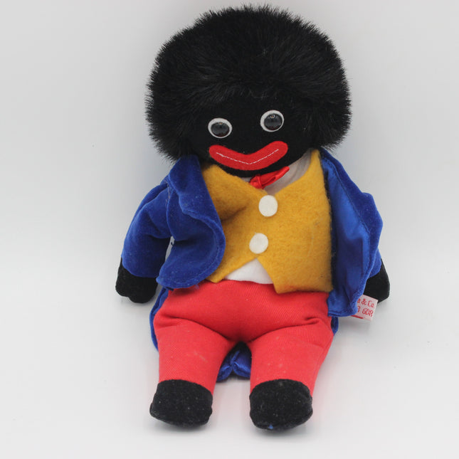 A vintage-style plush Golly doll with a black furry head, black face, red lips, a yellow vest, blue jacket, and red pants, photographed against a plain light background.