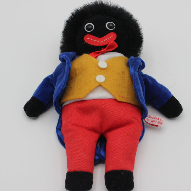 A plush toy Robertsons Golly doll with a black furry head and hands, wearing a blue jacket, yellow vest, red pants, and a red bow tie, photographed on a plain light background.