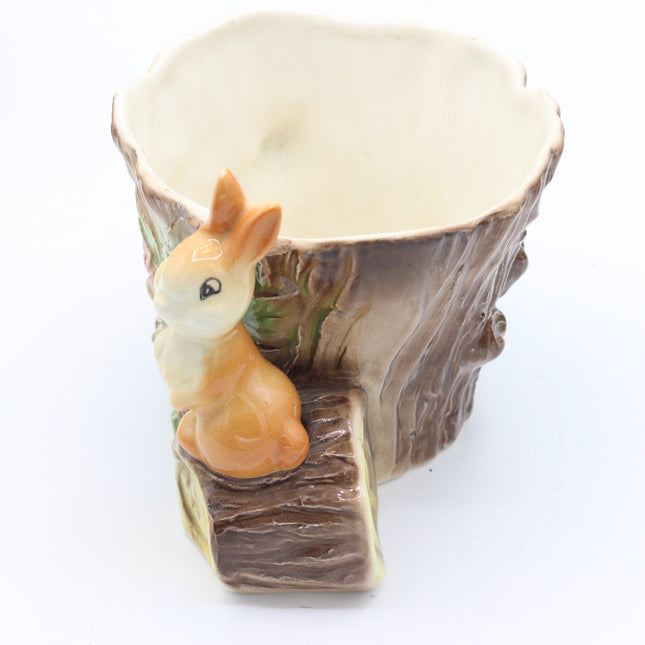 A ceramic planter shaped like a tree stump with a small orange and cream bunny figurine sitting on the front, photographed on a plain white background.
