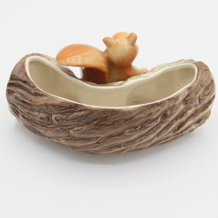A ceramic squirrel dish shaped like a tree hollow, featuring a brown bark-textured exterior and a small orange-brown squirrel figurine sitting inside the opening, shown on a plain white background.