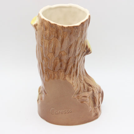 A ceramic mug shaped like a tree stump, featuring a textured bark pattern in brown and beige tones with a smooth base embossed with the brand name 'Caressa'.