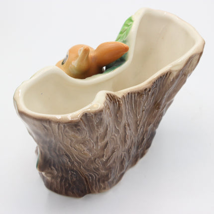 A ceramic planter shaped like a tree stump with a small orange animal figurine peeking out from the top, photographed on a plain white background.