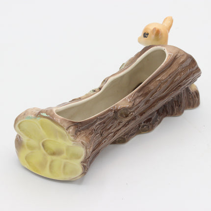 A ceramic planter shaped like a log with a small animal figurine perched on top, photographed on a plain white background.