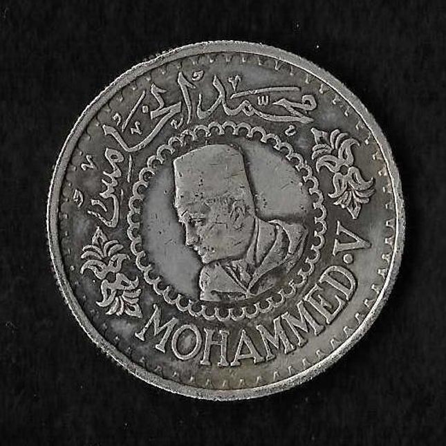 A round silver-colored coin featuring a profile portrait of Mohammed, surrounded by Arabic calligraphy and the word 'MOHAMMED' at the bottom, shown on a black background.
