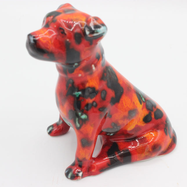 A glossy ceramic figurine of a sitting dog with a red, orange, and black marbled pattern, photographed on a plain white background.