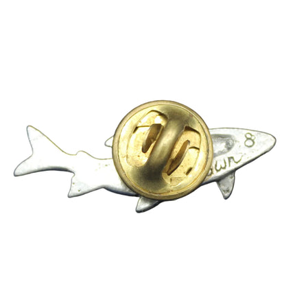 Gold and silver shark-shaped pin on a blue background