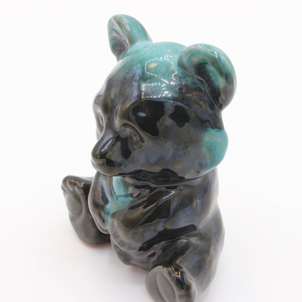 A small glossy ceramic figurine of a seated bear with a dark charcoal base and turquoise-blue glazed highlights, photographed on a plain white background.