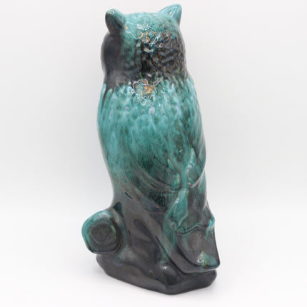A ceramic owl figurine in a glossy glaze, featuring a vibrant turquoise-green body with dark brown and black shading, sitting on a small base against a white background.