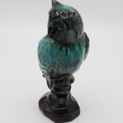 A ceramic owl figurine with a glossy glaze, featuring a teal and green body with dark black and brown accents, standing on a matching dark base against a plain white background.