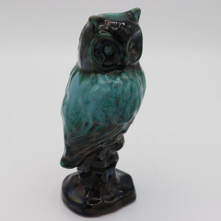A ceramic owl figurine with a glossy glaze, featuring a marbled pattern of teal green and dark black-brown tones, standing on a small base against a plain light gray background.