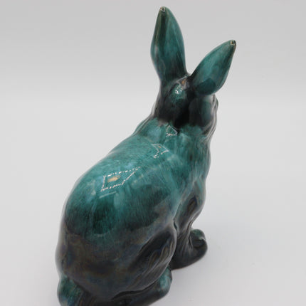 A ceramic rabbit figurine with a glossy teal and dark green glaze, shown from a rear three-quarter view on a light gray background.