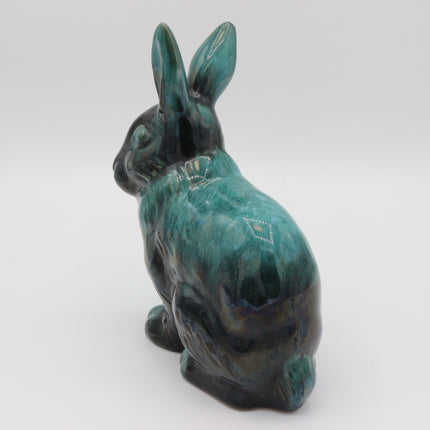 A ceramic rabbit figurine with a glossy teal and dark green glaze, shown from a rear three-quarter view on a light gray background.