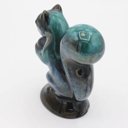 A small sculpted figurine of a squirrel in a sitting pose, made from polished stone with a glossy finish. The coloration is a mix of teal, blue, and dark brown, with a small white inlay detail on the rounded back.