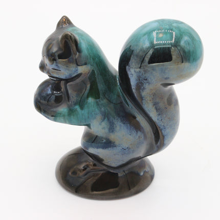 A glossy ceramic squirrel figurine with a blue, green, and black glazed finish, standing on a round base against a white background.