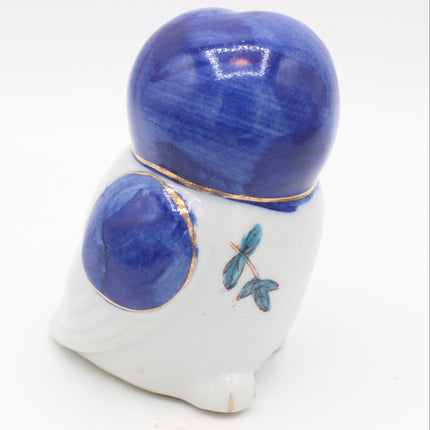 A small ceramic bird figurine with a glossy blue and white glaze, featuring gold trim and a painted blue-green leaf detail on its side, set against a plain white background.