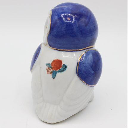 A ceramic owl figurine shown from the back, featuring a glossy white body, deep cobalt blue head and shoulder details, and a small painted red and blue flower accent on the back.