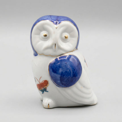 A small ceramic owl figurine with a glossy white body, a deep cobalt blue head and chest patch, and tiny gold accents around the eyes and edges, set against a plain white background.