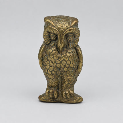 A small decorative owl figurine with a textured metallic gold finish, standing on a plain light gray background.