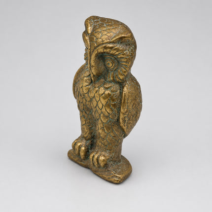 A small metallic owl figurine with a textured, aged gold finish, standing on a plain light gray background.