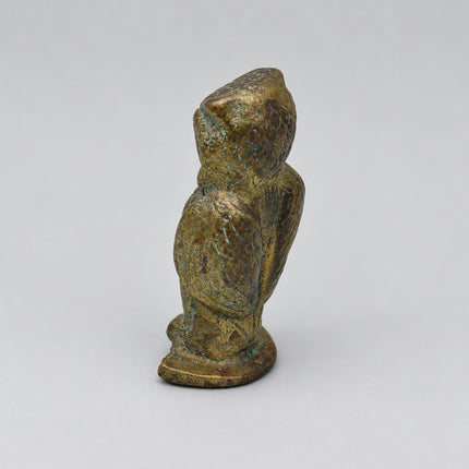 A small antique-style metallic figurine of a seated figure, shown from the back on a plain light gray background.