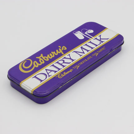 A rectangular purple Cadbury Dairy Milk chocolate tin with gold and white lettering, photographed on a light gray background.