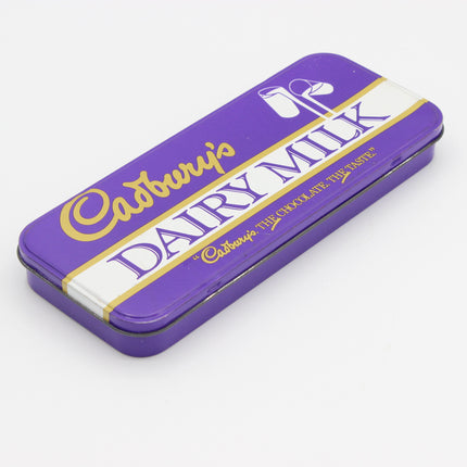 A purple Cadbury Dairy Milk chocolate tin with gold and white lettering, shown at an angle on a light gray background.