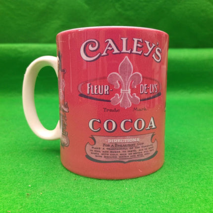 A vintage-style red ceramic mug featuring Caley's Cocoa branding with a white handle, set against a bright green background.