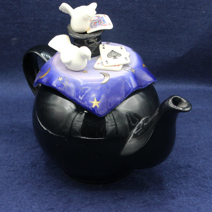 Black teapot with a purple lid featuring cards and birds on a blue background