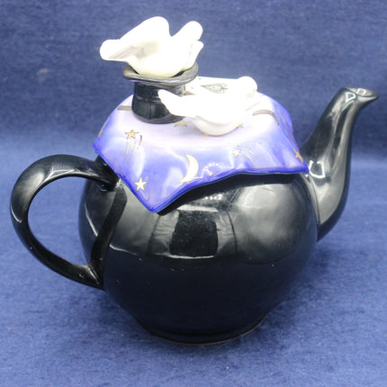 Black teapot with decorative lid featuring white doves on a blue background
