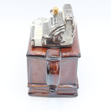 A ceramic novelty mug shaped like a vintage cash register, featuring a glossy brown body with a metallic silver register top and a small gold button, shown on a white background.