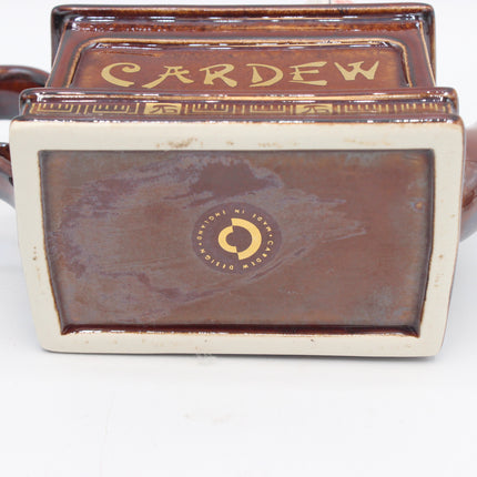 Close-up of the base of a ceramic card deck box, showing a brown glazed interior with gold lettering that reads 'CARD EW' and a circular gold logo in the center, set against a plain white background.