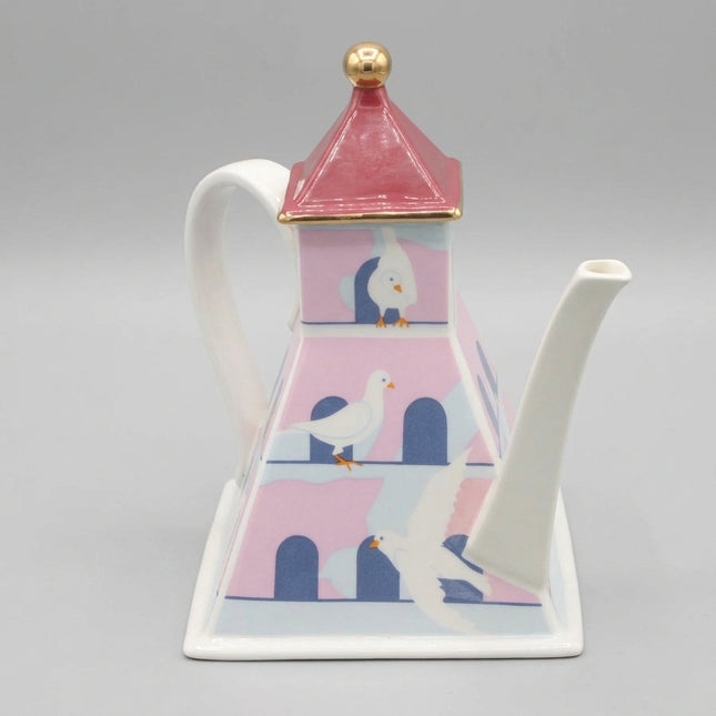 Decorative teapot with a bird house design on a dark blue background