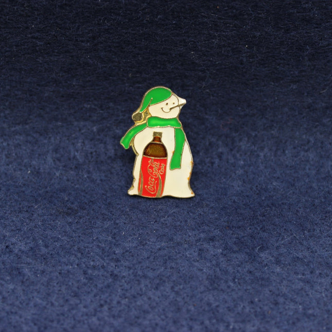 Snowman pin badge with a bottleof coca-cola on a dark blue background