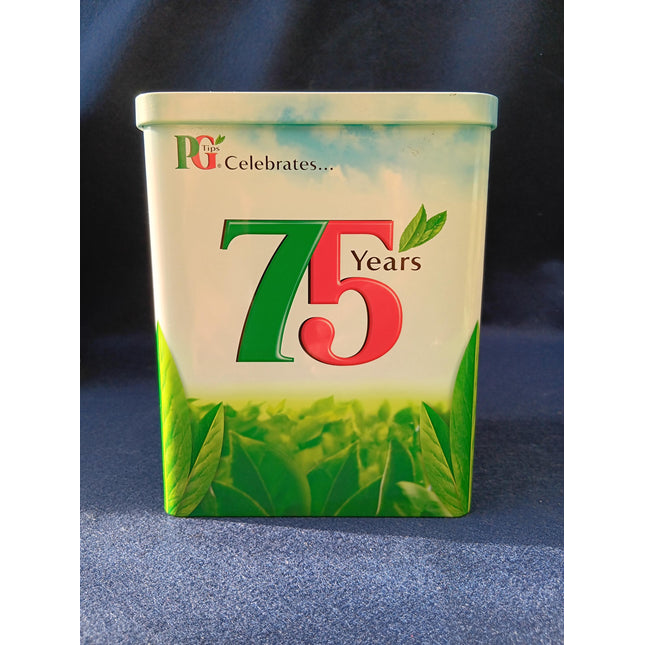 A rectangular metal tin with rounded corners celebrating 75 years, featuring a white top half with green sky and blue gradient, a red and green '75' design, and a green tea leaf field at the bottom. The text 'PG Celebrates.