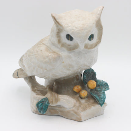 A vintage ceramic owl figurine perched on a branch with green leaves and small yellow berries, shown against a plain white background.