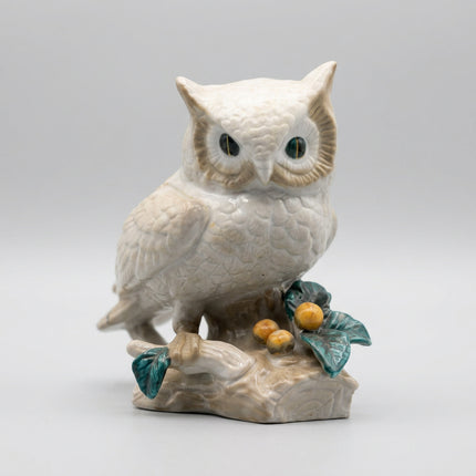 A vintage ceramic owl figurine perched on a branch with green leaves and small yellow berries, shown against a plain white background.