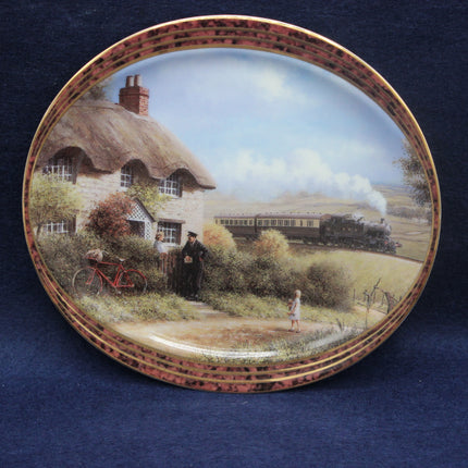Decorative plate with a scenic painting of a thatched cottage, bicycle, and steam train.