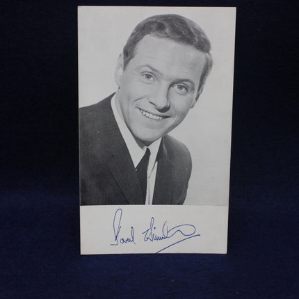 Black and white photo of a smiling man with a signature on a dark background