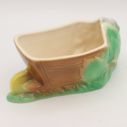 A ceramic planter shaped like a covered wagon on a grassy hill, featuring a tan-brown wagon body with green and yellow grass accents, photographed on a plain white background.